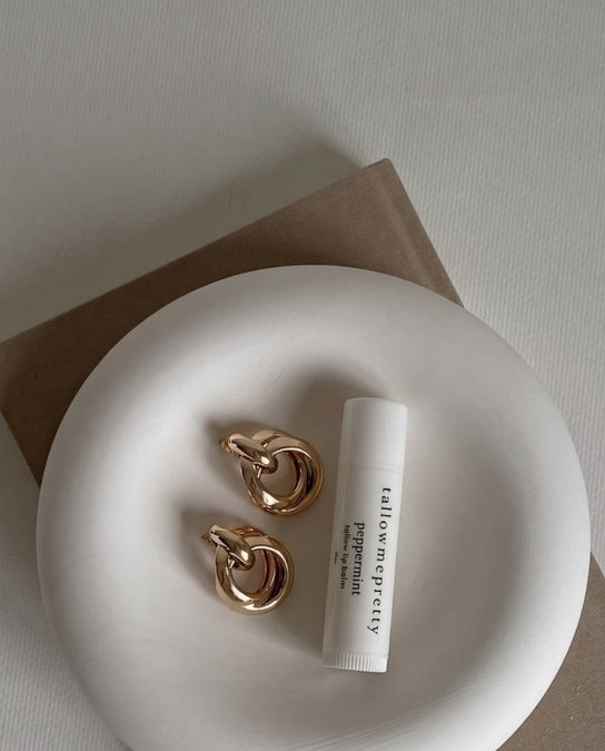 Tallow lip balm vs petroleum jelly: Tallow Me Pretty peppermint lip balm on a white plate with gold earrings