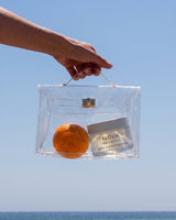 Whipped tallow body moisturizer for legs: Ageless Firming Body Cream and an orange in a clear bag against a blue sky
