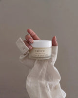 Hand cream with simple ingredients: hand wrapped in linen holding a jar of Tallow and Honey Balm