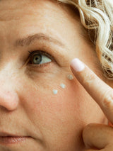 Cream for crow's feet: woman dotting blue tallow cream under her eye