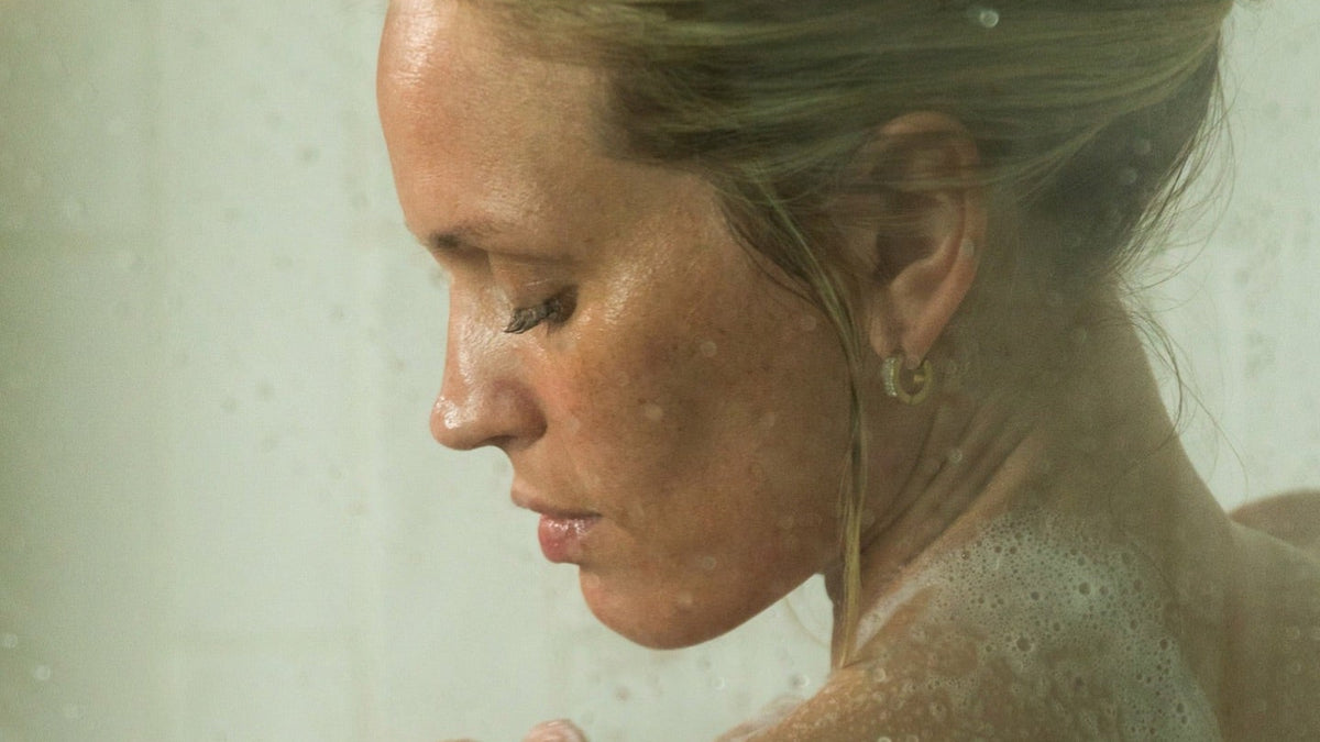Body cloud cream vs regular moisturizers: woman rinsing in a steamy shower with her hand on her shoulder
