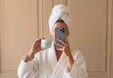 Skincare for your 30s: woman in a white robe and hair towel taking a mirror selfie with Ageless Cloud Cream