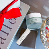 Tallow skincare products including a jar and tube on a textured surface with a decorative box in the background.