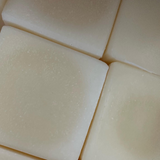Close-up of several stacked bars of Tallow Me Pretty unscented tallow soap, showcasing their uniform ivory color and subtly speckled texture, evoking a sense of pure, clean simplicity.