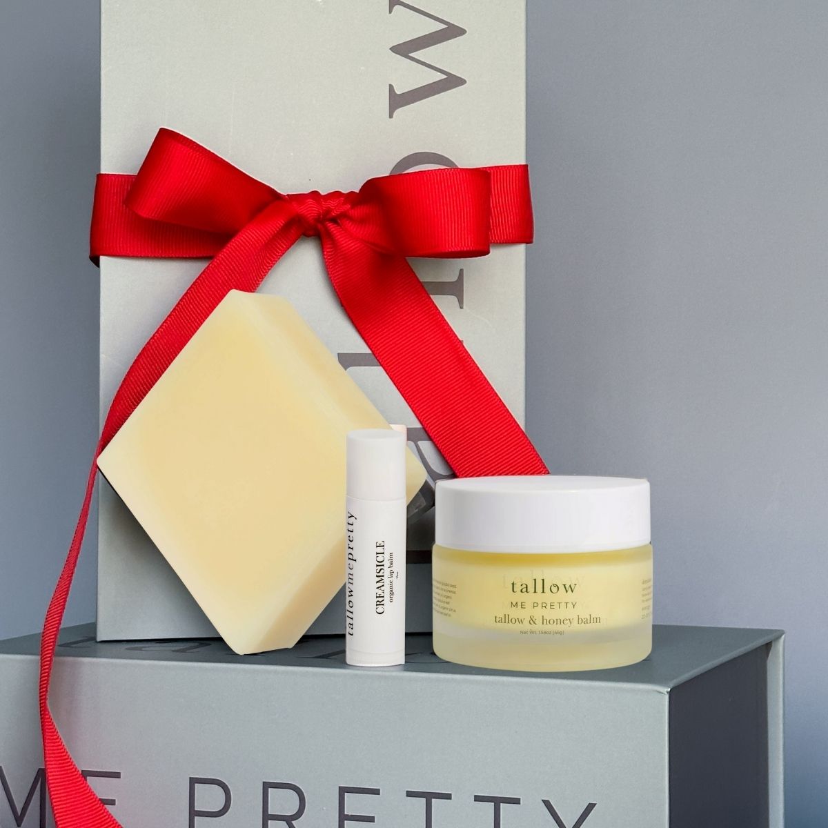 Cosmetic products including a jar, bar of soap, and bottle on a gray surface with a red ribbon.