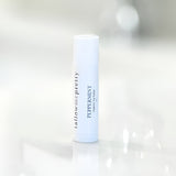 A slim, upright peppermint organic lip balm stick with a white cap stands against a softly blurred background. The side of the tube is labeled in a simple, elegant font 'tallow me pretty' above the words 'PEPPERMINT organic lip balm', indicating a natural skincare product. The tube is positioned on a reflective surface, conveying a clean and pure aesthetic.
