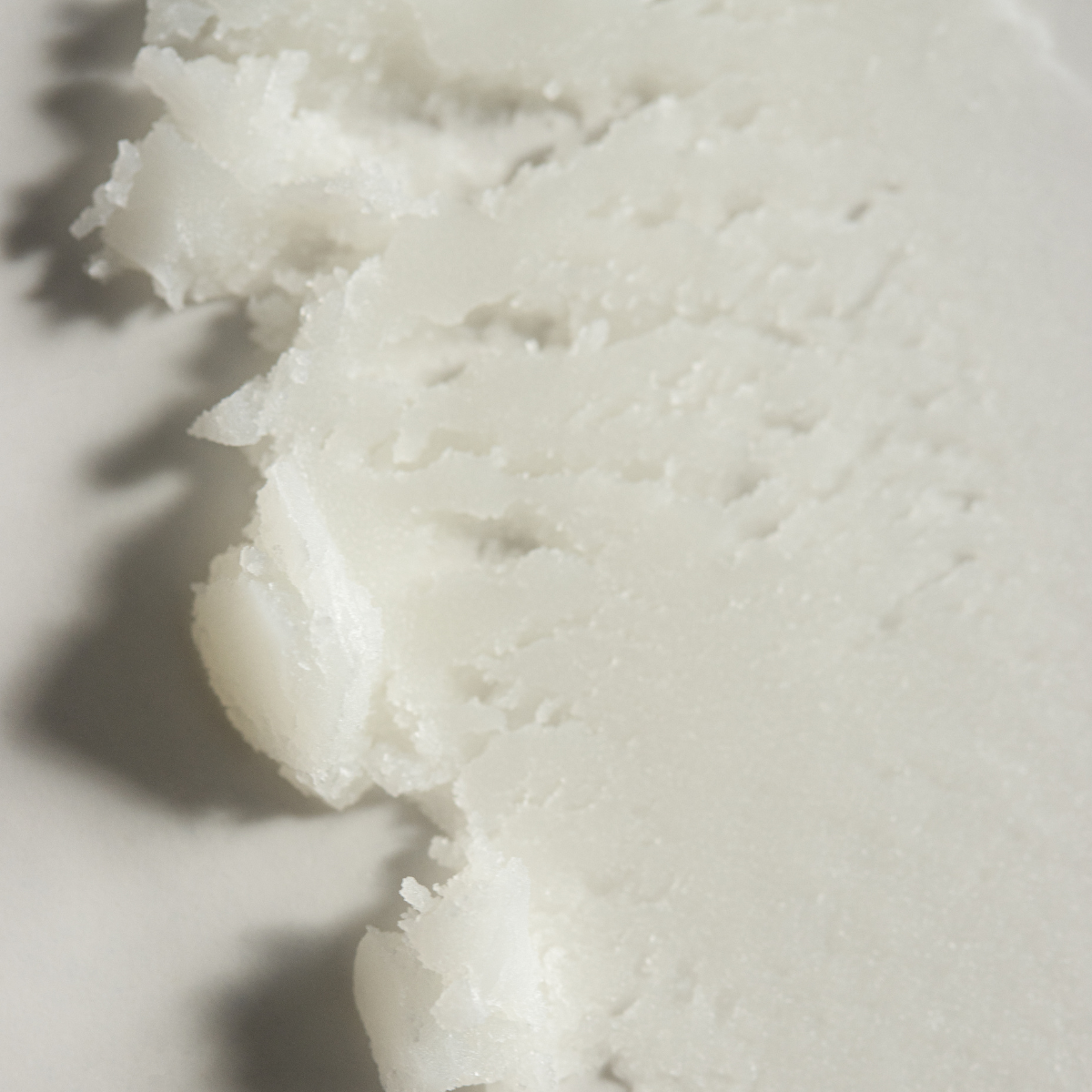 A close-up of a white, semi-translucent solid cosmetic or skincare product with a textured, slightly melted surface on a light background.
