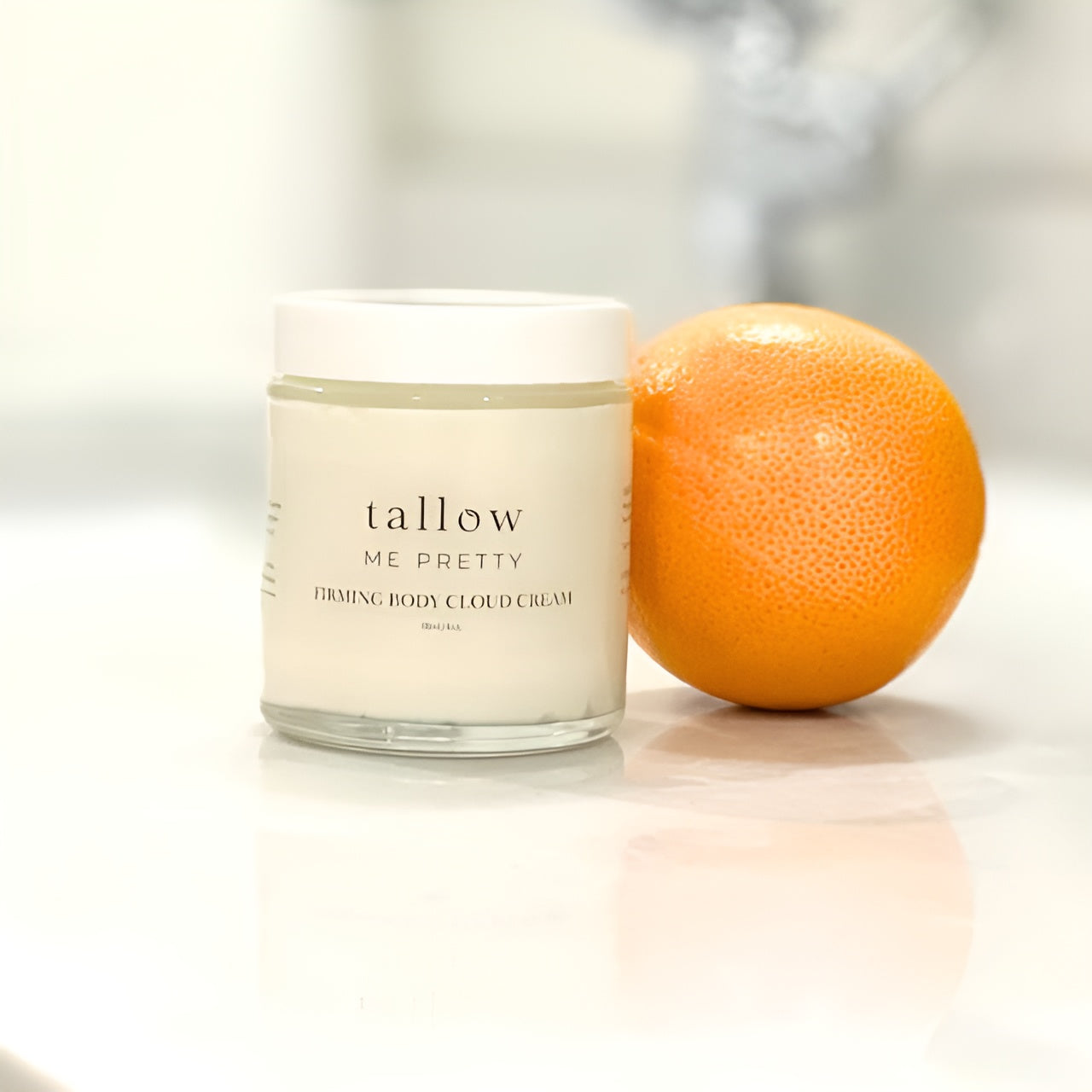 'Tallow Me Pretty' body cream jar with fresh orange, highlighting natural ingredients.