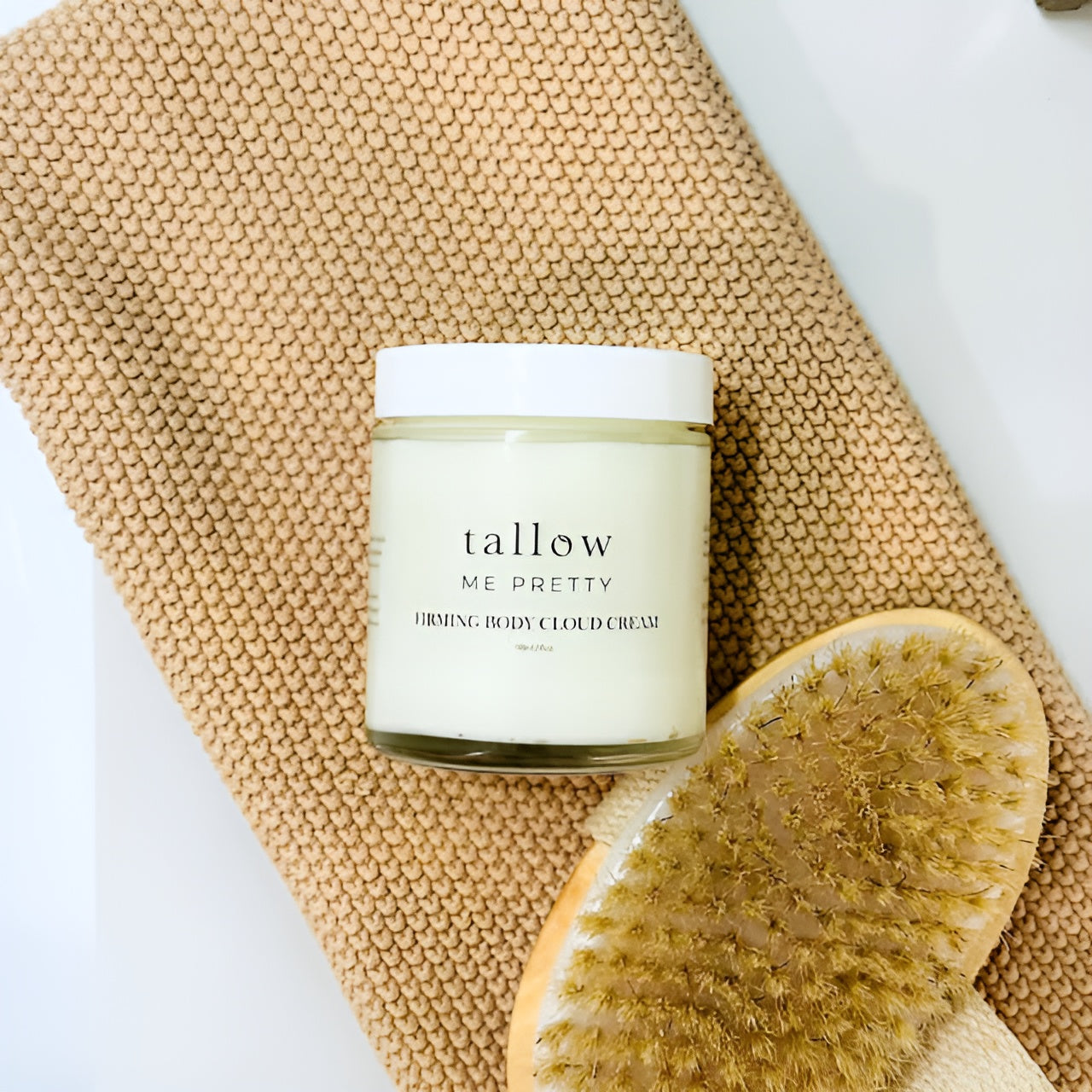 Firming Body Cloud Cream is displayed on an earthy knitted towel with a spa dry brush.