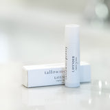 Tallow Me Pretty Lavender Organic Lip Balm next to its elegant white packaging on a soft, blurred background.