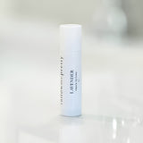 A Tallow Me Pretty Lavender Organic Lip Balm in a white, roll-up tube displayed on a glossy white surface. The tube's label is printed in elegant black typography, highlighting the organic and natural qualities of the product.