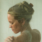 Woman under a shower with water droplets on her skin and hair.