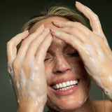 Woman with soapy hands on her face against a dark background