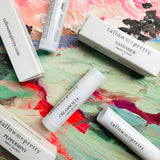 Array of Tallow Me Pretty organic lip balms in Creamsicle, Lavender, and Peppermint, artistically displayed over a colorful painted background, conveying the brand's artisanal approach to natural lip care.
