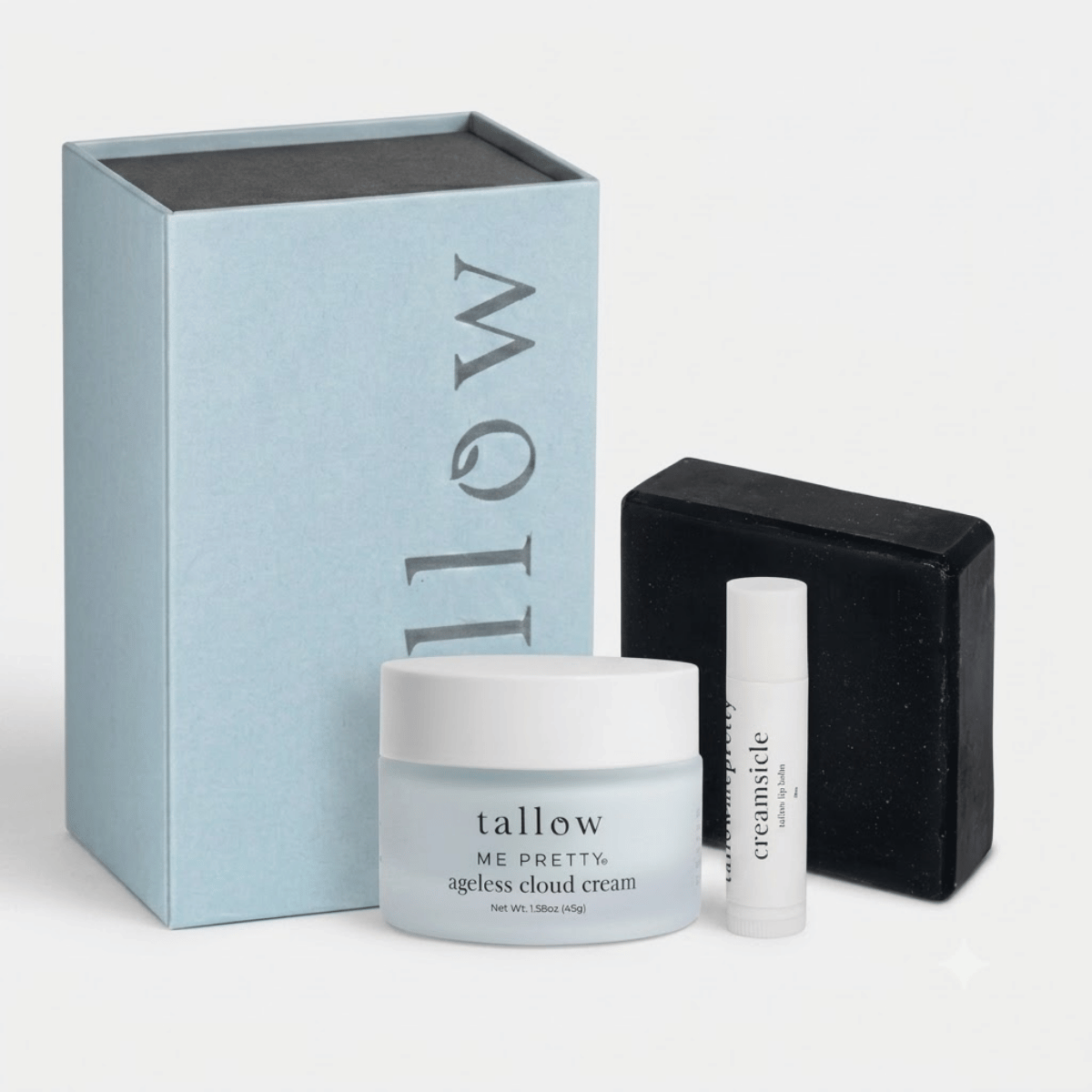 A skincare gift set featuring a large light blue box with vertical 'tallow' branding, a frosted white jar of Me Pretty Ageless Cloud Cream, a small white lip balm tube labeled 'creamsicle', and a black rectangular box, all arranged on a clean white background.