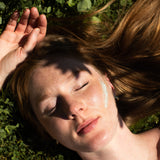 Person lying on grass with eyes closed, hand on head and tallow on cheek.